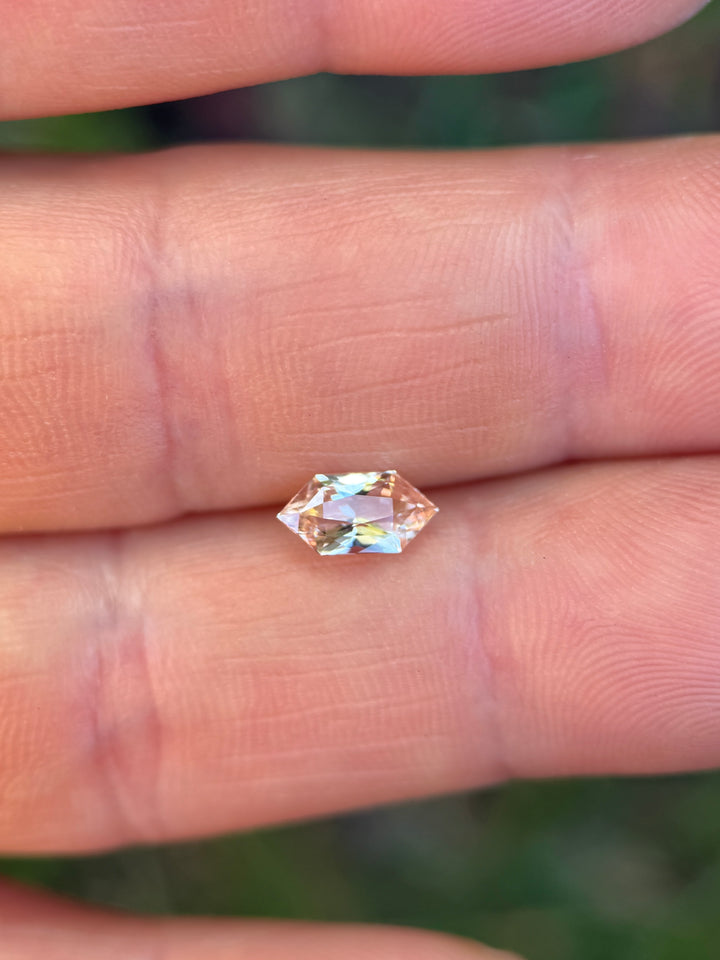 Salmon pink peach sapphire on fingertip showing size and soft color tones, elongated hexagon loose gemstone.