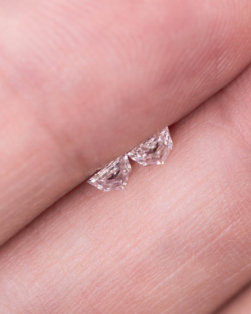 Close-up image of a matching pair of 0.18 carat D color Cadillac cut diamonds from South Africa displayed on a fingertip. The stones exhibit exceptional clarity, precision faceting, and natural brilliance.