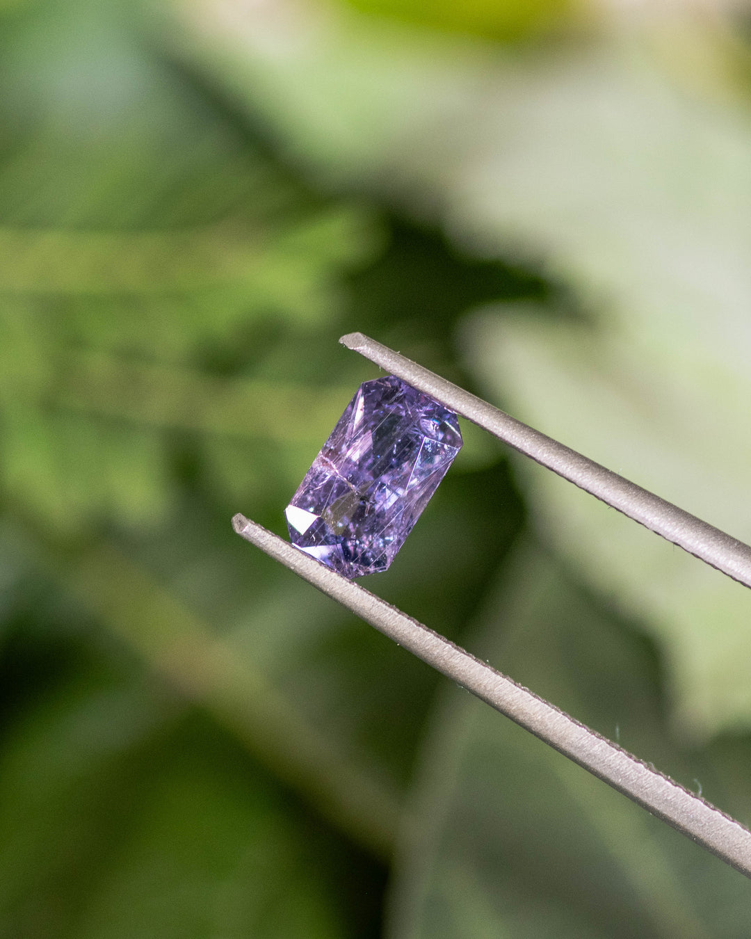 Close-up of 0.94CT gray purple sapphire held in tweezers, capturing its elongated radiant cut and fine light dispersion under natural lighting, ethically sourced unheated gemstone from Umba River Valley, Tanzania.