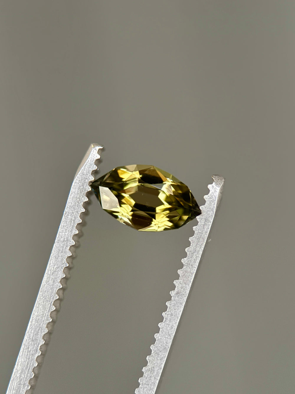 0.94-carat olive green tanzanite displayed on a natural background, emphasizing the antique style cut and internal color zoning. Untreated Tanzanite from Merelani Hills shown upright to reveal sparkle and proportions.