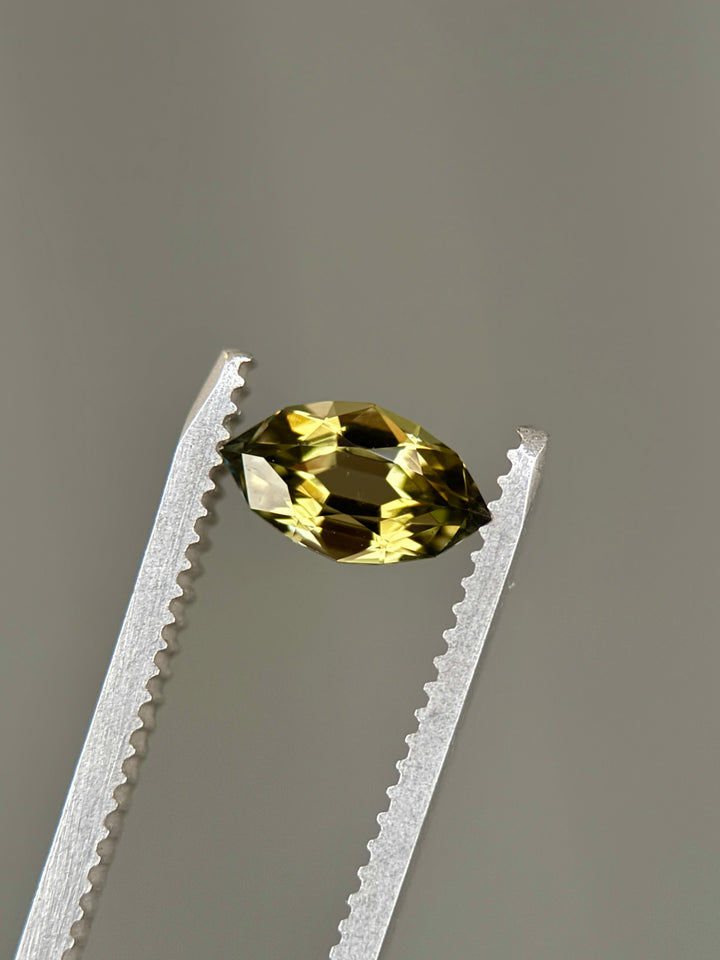 0.94-carat olive green tanzanite displayed on a natural background, emphasizing the antique style cut and internal color zoning. Untreated Tanzanite from Merelani Hills shown upright to reveal sparkle and proportions.