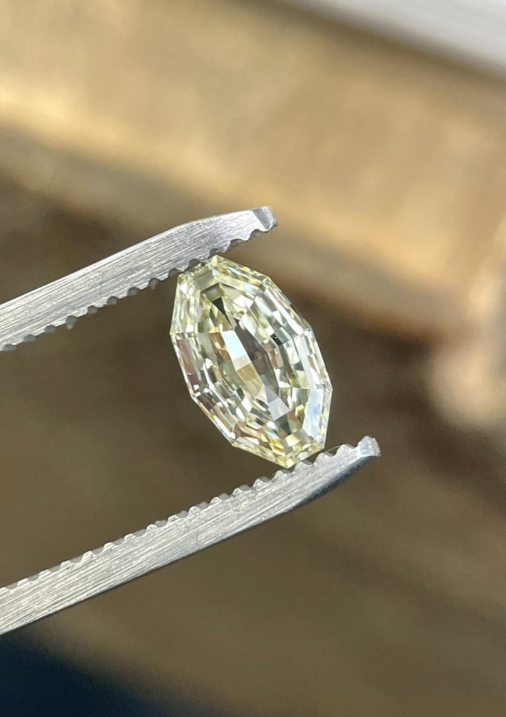 Close-up of a natural 0.99 carat VVS1 clarity light yellow diamond held by gem tweezers under soft light. The antique-style moval step cut reveals subtle color and intricate craftsmanship, ethically sourced from Gahcho Kué, Canada.