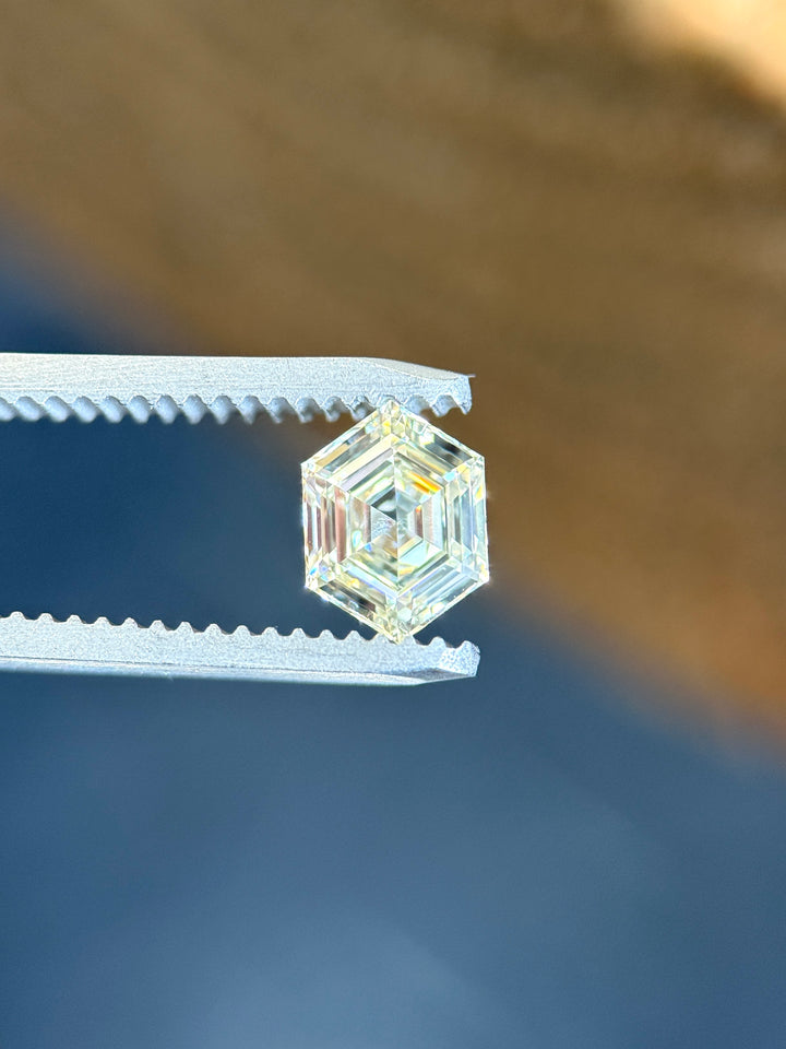 1.01 carat hexagonal step cut diamond from Gahcho Kué, Canada, held in gem tweezers under natural light. The O–P color VVS2 clarity diamond showcases sharp symmetry and a radiant geometric pattern.