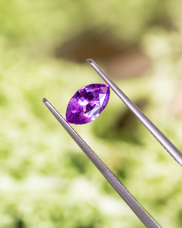Close-up of 1.01 carat purple and pink sapphire held in tweezers, highlighting the brilliance and symmetry of its marquise cut facets, unheated gem from Sakaraha, Madagascar.