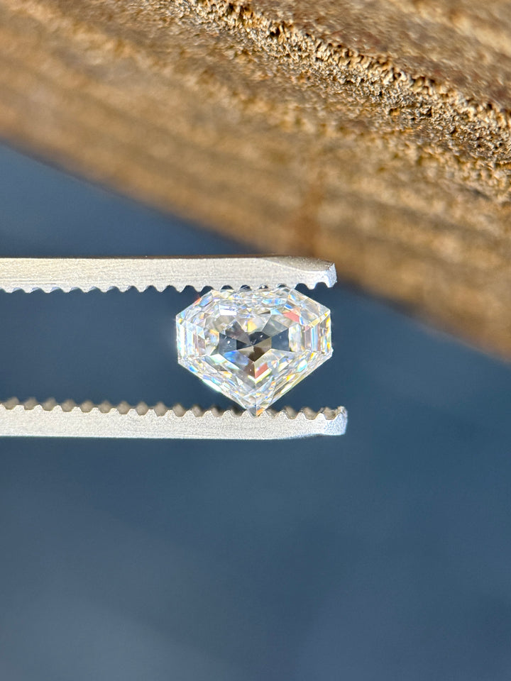 1.01 carat E color SI1 clarity diamond from Gahcho Kué, Canada, held in tweezers under natural light. The shield step cut reveals crisp reflections and fine craftsmanship in this untreated Canadian gem.