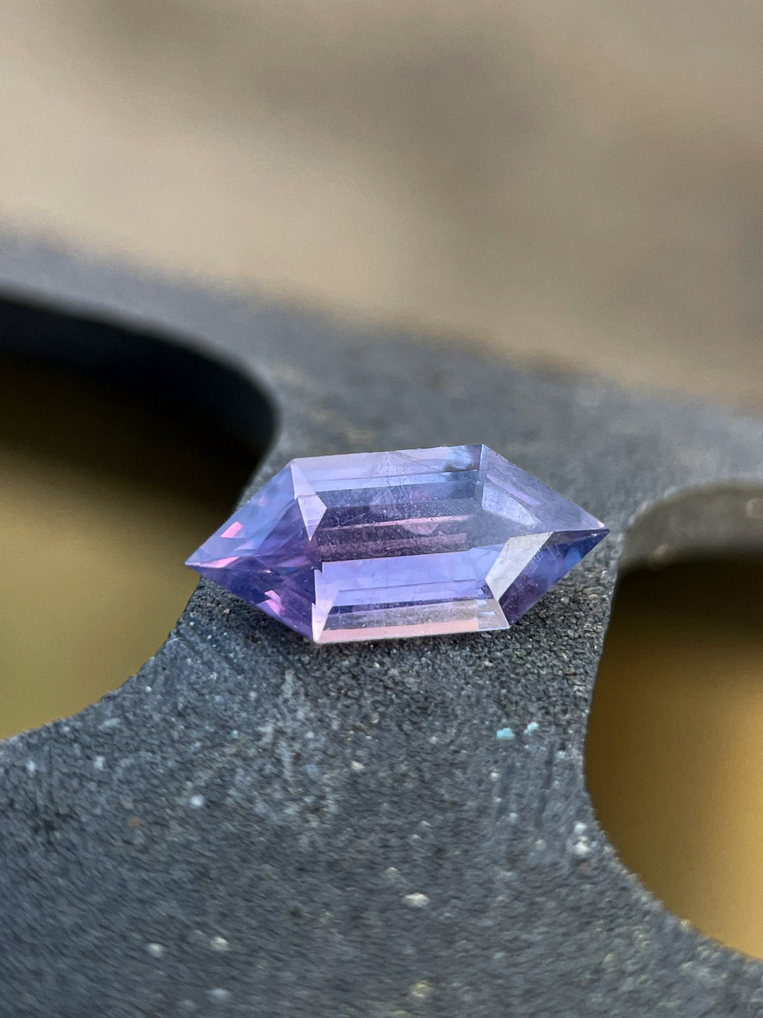 Close-up view of a 1.01-carat royal purple and pink sapphire resting on a textured surface, showcasing its hexagonal step-cut brilliance.