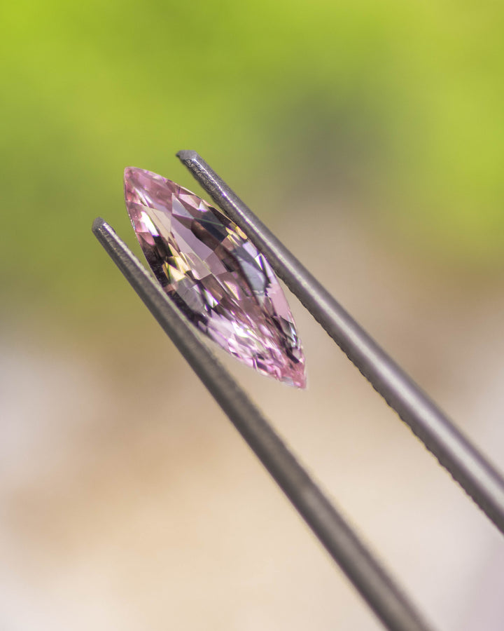 Macro photo of 1.03CT blush pink sapphire held delicately in gemstone tweezers under natural light, highlighting its fine faceting and vibrant sparkle from the precision marquise mixed cut, heated sapphire from Sakaraha, Madagascar.