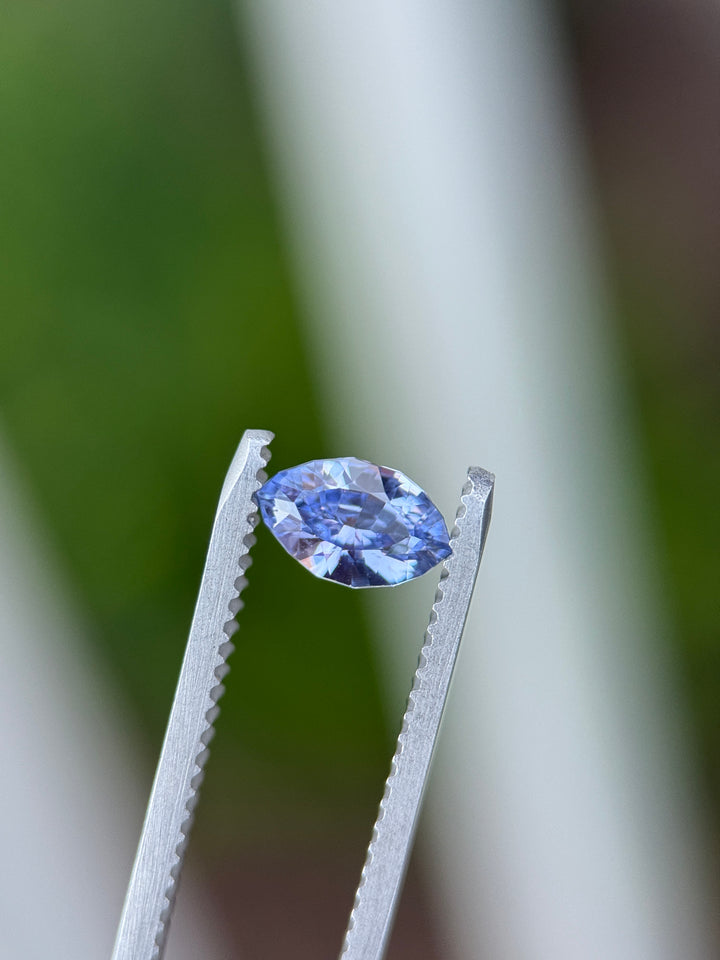 Macro image of 1.03CT indigo-purple sapphire held in gemstone tweezers under natural light, showing fine facets and vivid reflections from the precision marquise mixed cut, unheated sapphire from Sakaraha, Madagascar.