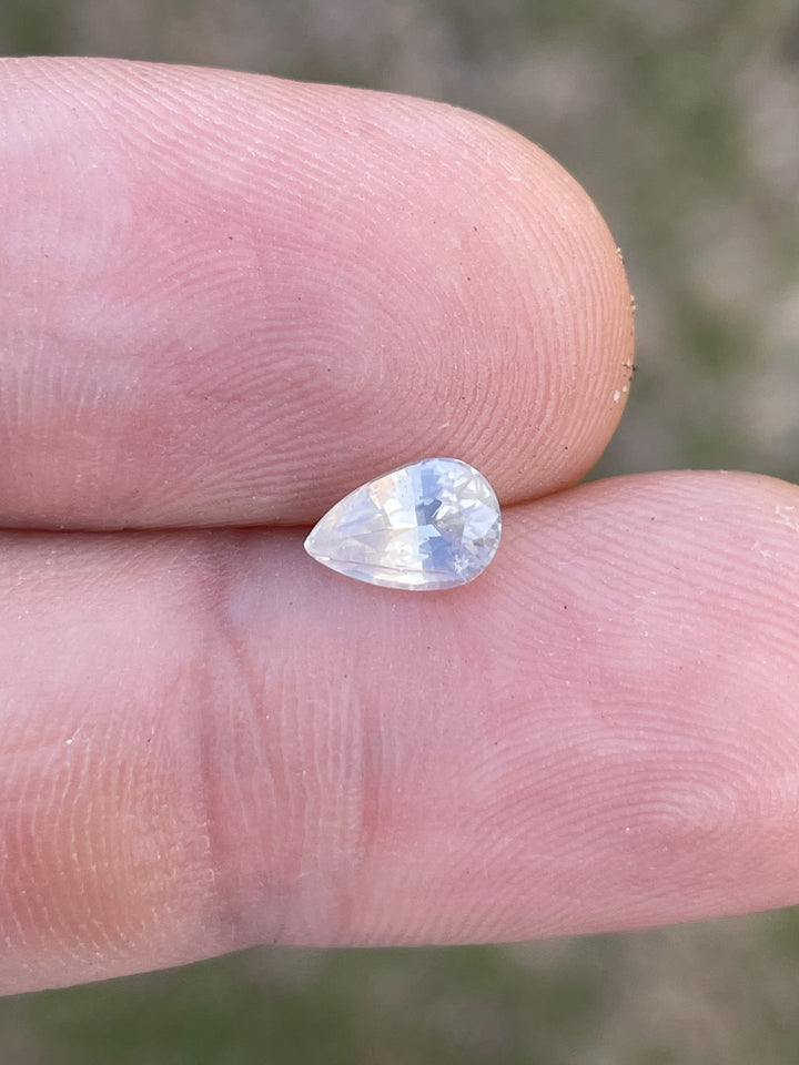 Close-up of a 1.05-carat pale yellow sapphire held between fingers, showcasing its custom shield cut and clarity.