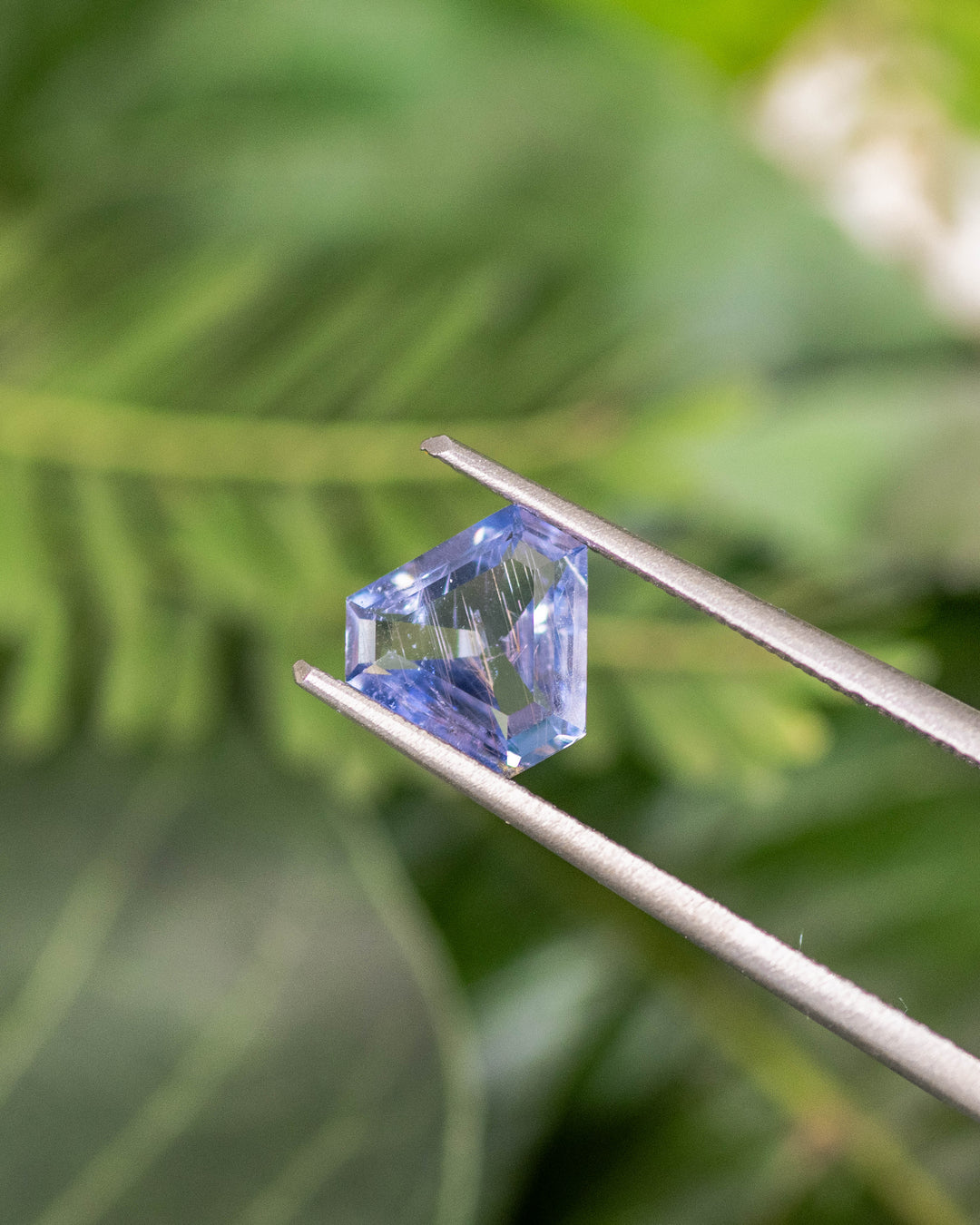 1.05CT violet aqua blue sapphire held in gemstone tweezers, highlighting intricate triangular facets and transparent luster of its custom cut corner trillion mix cut, unheated gem from Umba River, Tanzania.