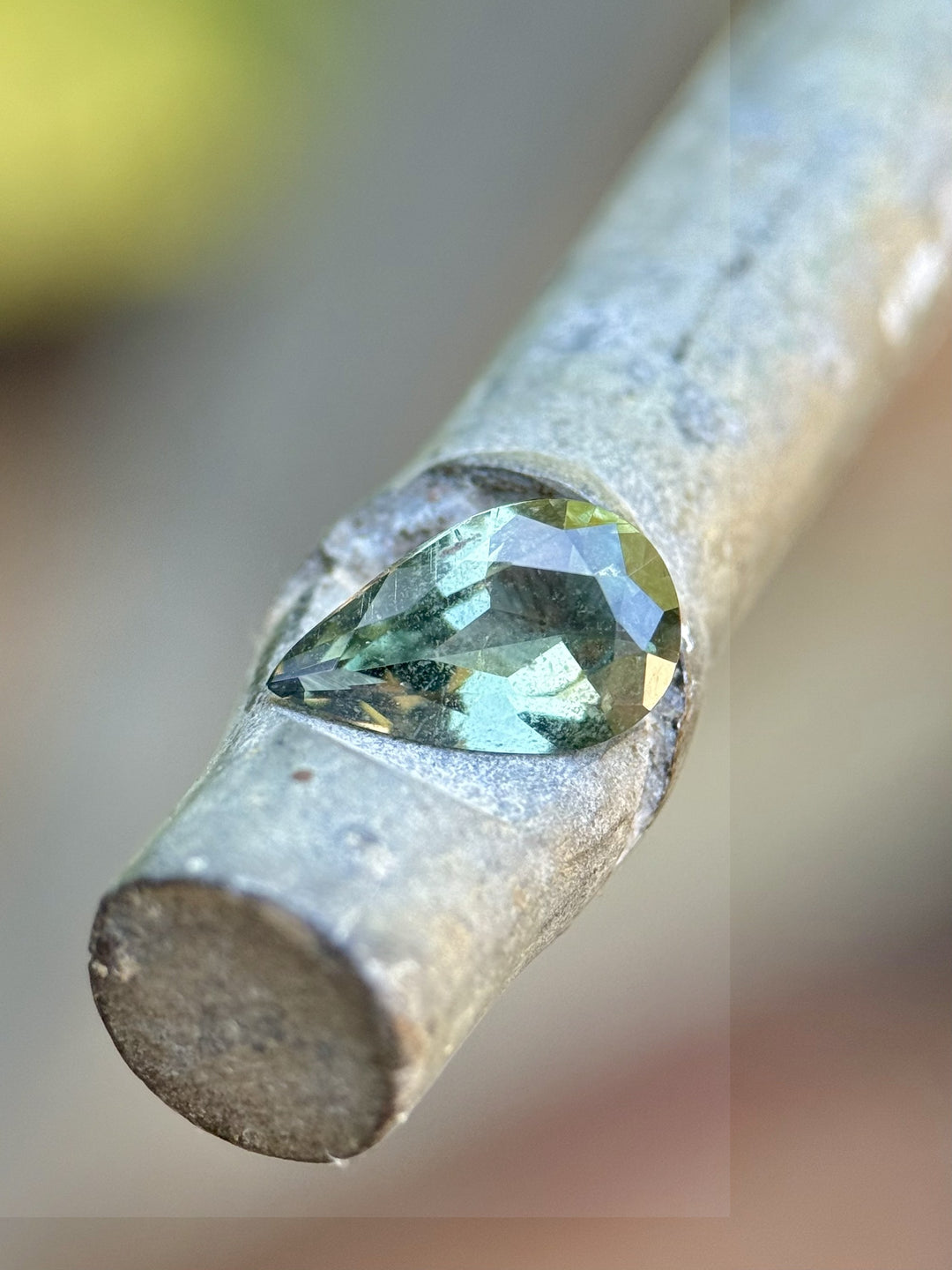 Natural 1.06ct pear-shaped teal green sapphire shown in angled profile on gray surface, untreated gemstone from Umba River, Tanzania