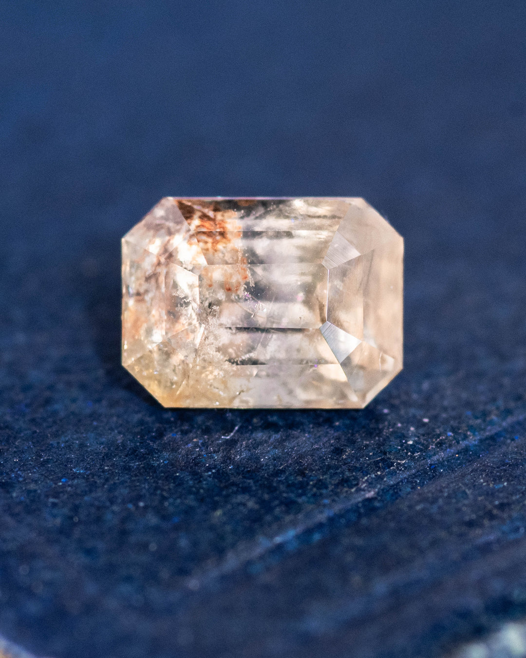 1.11CT grey teal yellow parti sapphire placed on deep blue surface, highlighting its transparent body, step-cut facets, and natural unheated clarity, custom emerald cut gem from Umba River Valley, Tanzania.
