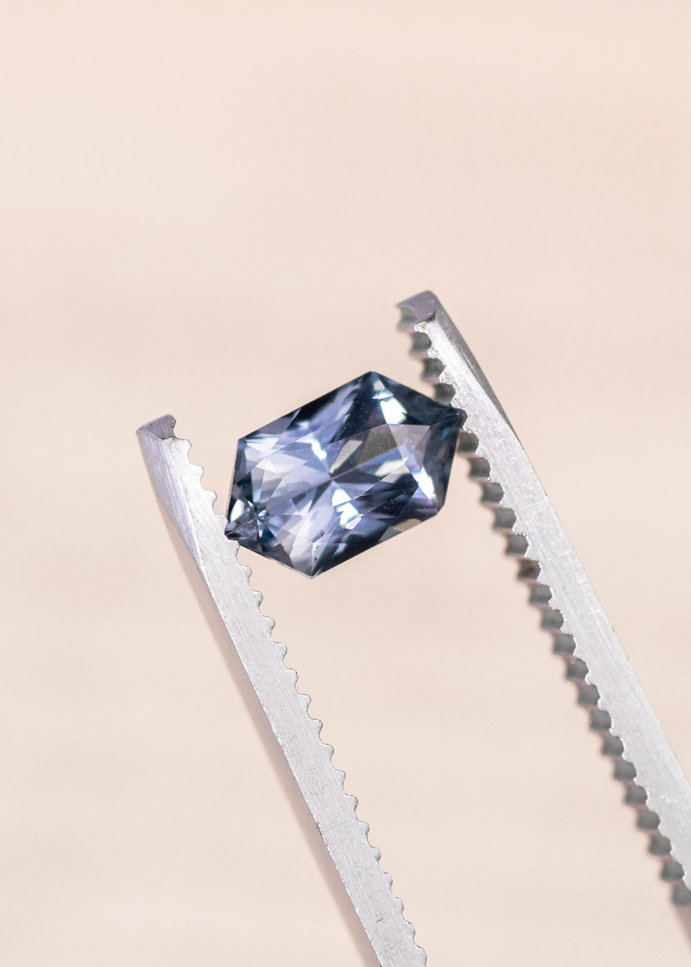 Seafoam grey blue sapphire held in precision gem tweezers, elongated hexagon mix cut displaying sharp facet reflections and balanced proportions, 1.11 carat unheated sapphire from Madagascar