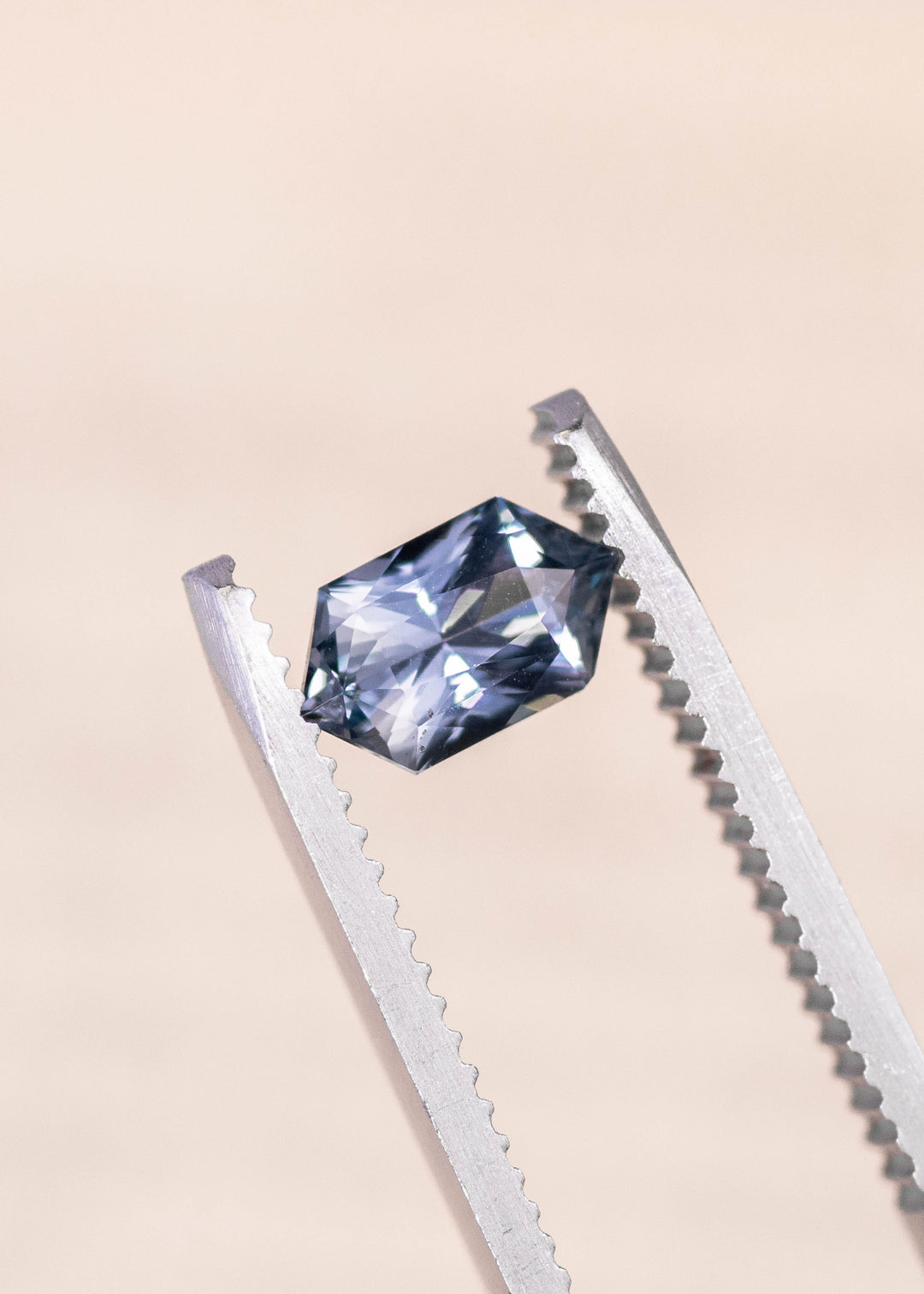 Seafoam grey blue sapphire held in precision gem tweezers, elongated hexagon mix cut displaying sharp facet reflections and balanced proportions, 1.11 carat unheated sapphire from Madagascar