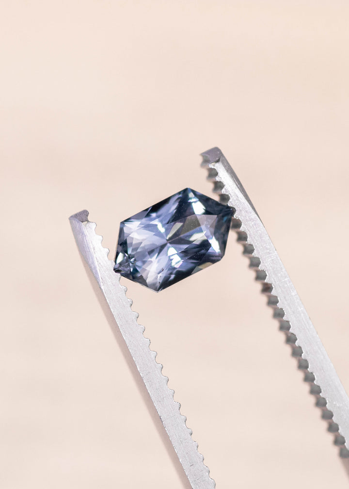 Seafoam grey blue sapphire held in precision gem tweezers, elongated hexagon mix cut displaying sharp facet reflections and balanced proportions, 1.11 carat unheated sapphire from Madagascar