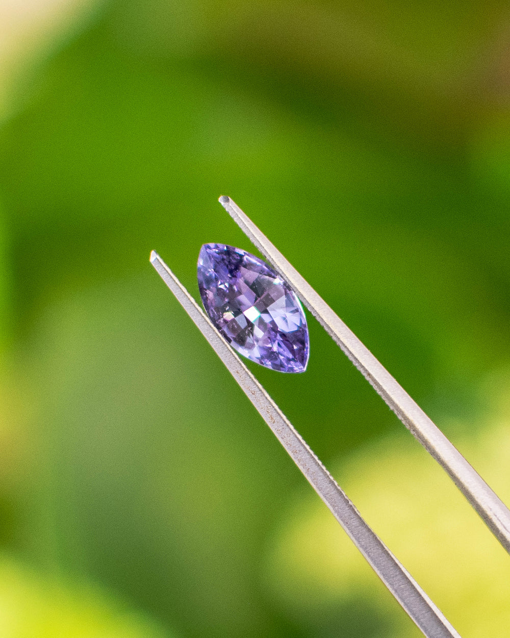 Close-up of 1.15CT lavender purple sapphire held in gemstone tweezers, showing the symmetry and brilliance of the precision marquise mixed cut under natural sunlight, unheated gem from Sakaraha, Madagascar.