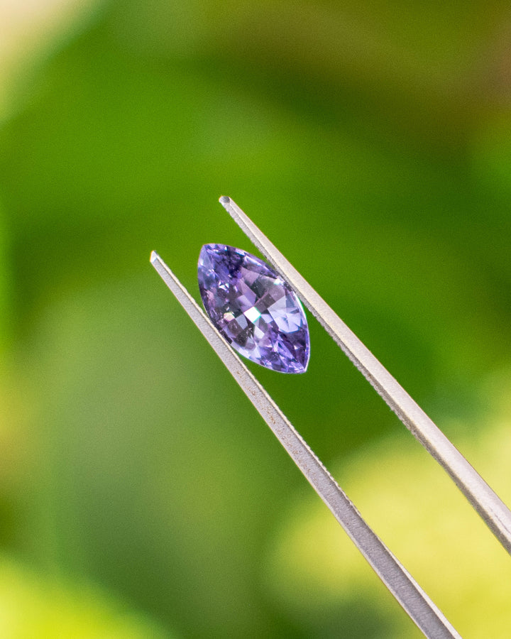 Close-up of 1.15CT lavender purple sapphire held in gemstone tweezers, showing the symmetry and brilliance of the precision marquise mixed cut under natural sunlight, unheated gem from Sakaraha, Madagascar.