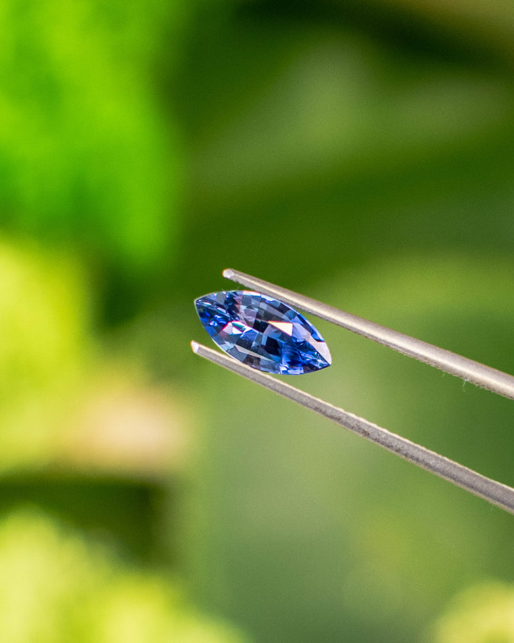 Macro image of 1.24CT vivid blue sapphire held in gemstone tweezers under natural sunlight, revealing rich blue saturation and fine craftsmanship of the precision marquise mixed cut, unheated sapphire from Sakaraha, Madagascar.