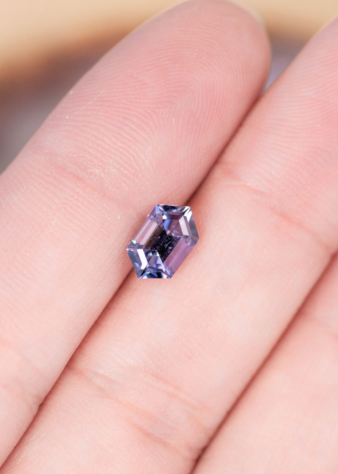 1.24 carat teal blue purple Tanzanite step cut hexagon resting on fingers showing precision faceting and color shift from Merelani Hills Tanzania
