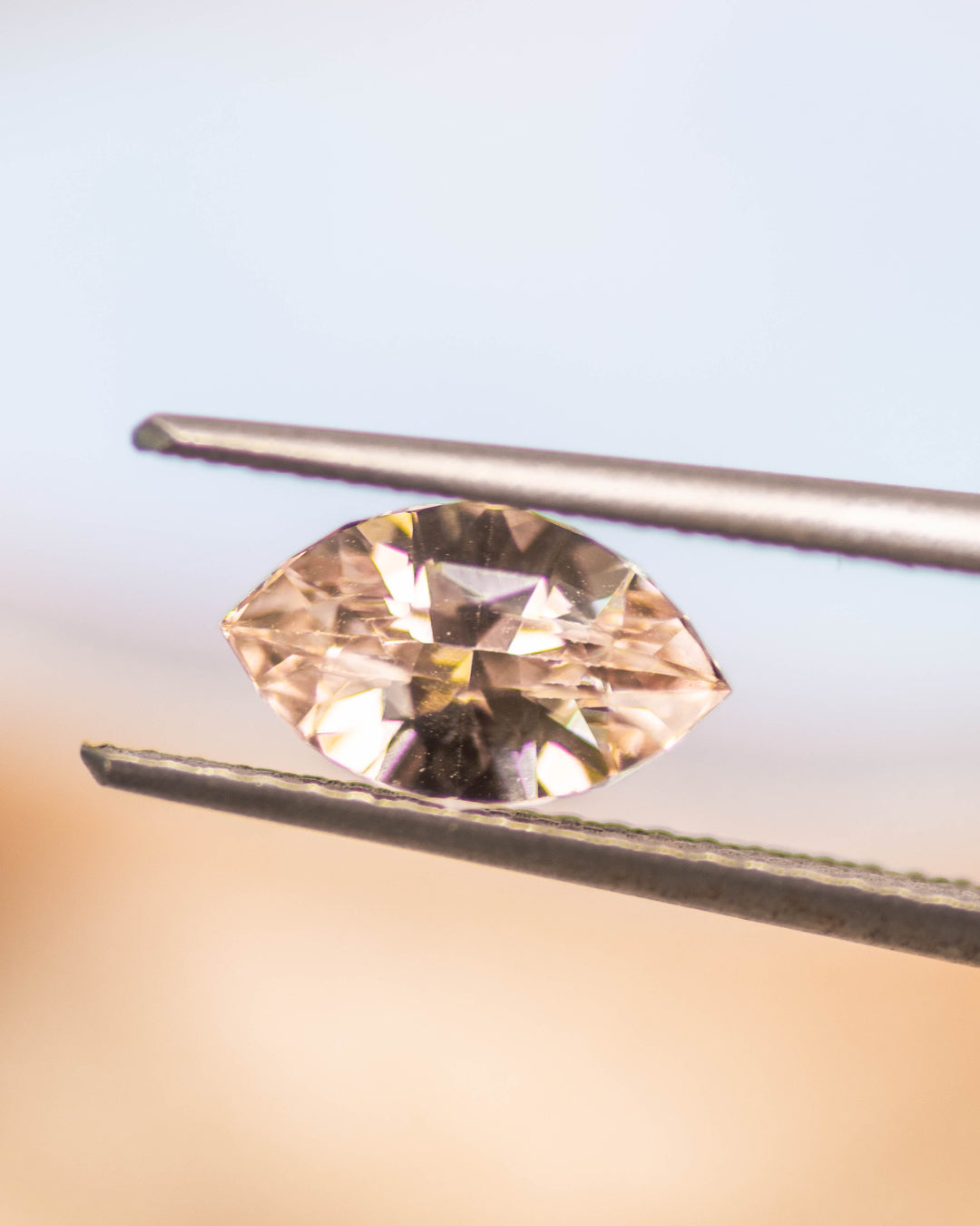 Macro image of 1.28CT peach sapphire held in gemstone tweezers under natural light, highlighting delicate sparkle and facets of the precision marquise mixed cut, unheated sapphire from Sakaraha, Madagascar.