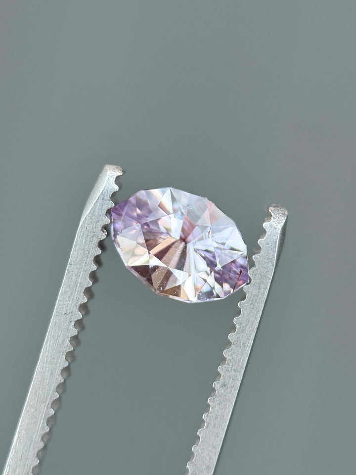 Macro close-up of 1.32CT pink, purple, and lilac sapphire held in gemstone tweezers, highlighting its brilliance and faceted reflections in a precision marquise mixed cut, unheated sapphire from Sakaraha, Madagascar.