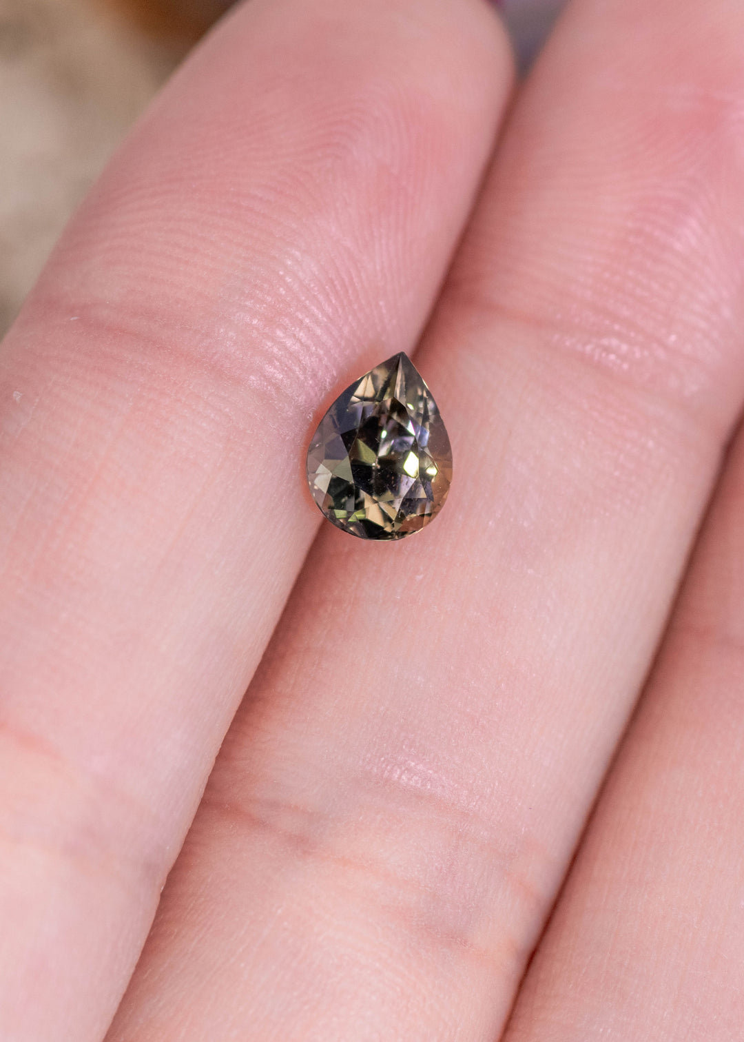 1.32 carat pear brilliant Tanzanite resting on fingers showing green brown purple color shift and precise brilliant faceting from Merelani Hills Tanzania