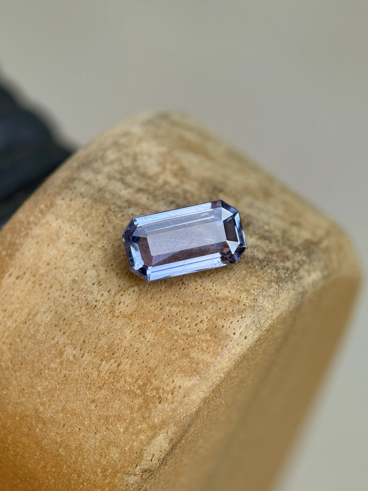 Unheated 1.41 carat Umba River sapphire with violet and blue hues in modified emerald cut resting on wooden surface