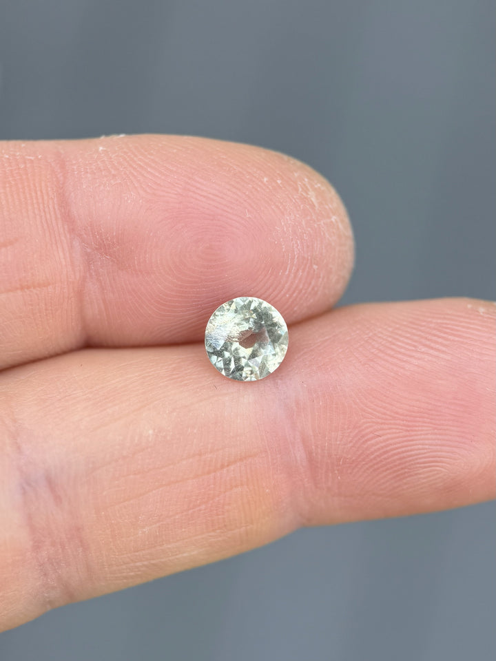 Round 1.42-carat untreated Tanzanian sapphire resting on fingertip, highlighting its vintage old mine cut and opalescent body color.
