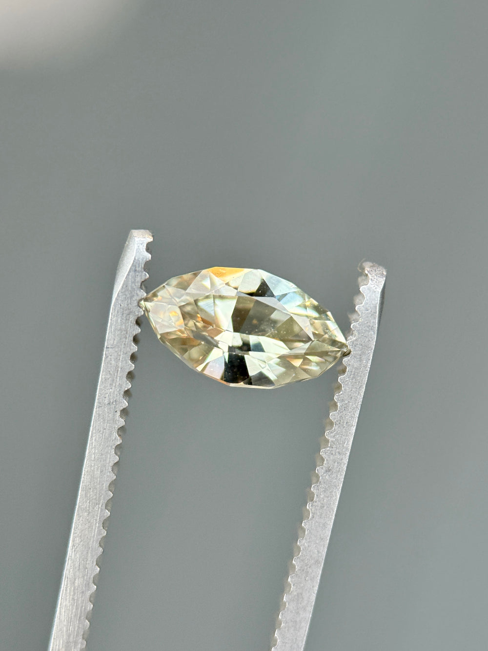 Macro image of 1.61CT yellow sapphire held in gemstone tweezers under soft lighting, highlighting brilliance, clarity, and symmetry of the precision marquise mixed cut, unheated sapphire from Sakaraha, Madagascar.