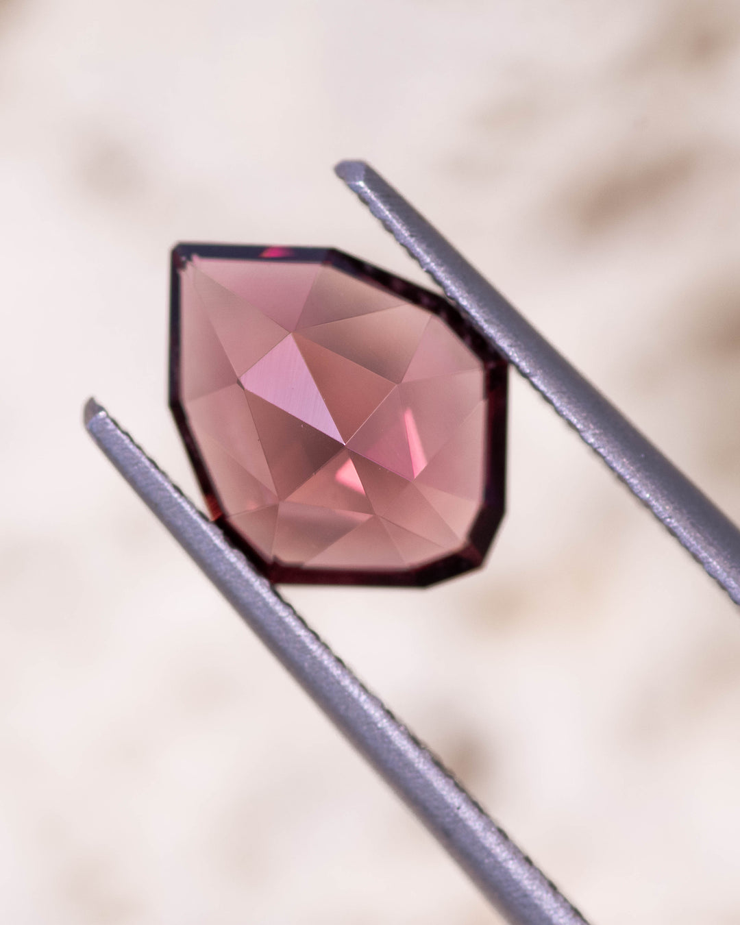 Close-up image of 1.66CT red orange garnet held in gemstone tweezers under natural light, capturing the luster, symmetry, and reflective brilliance of the custom geometric rose cut shield, unheated garnet from Kenya.