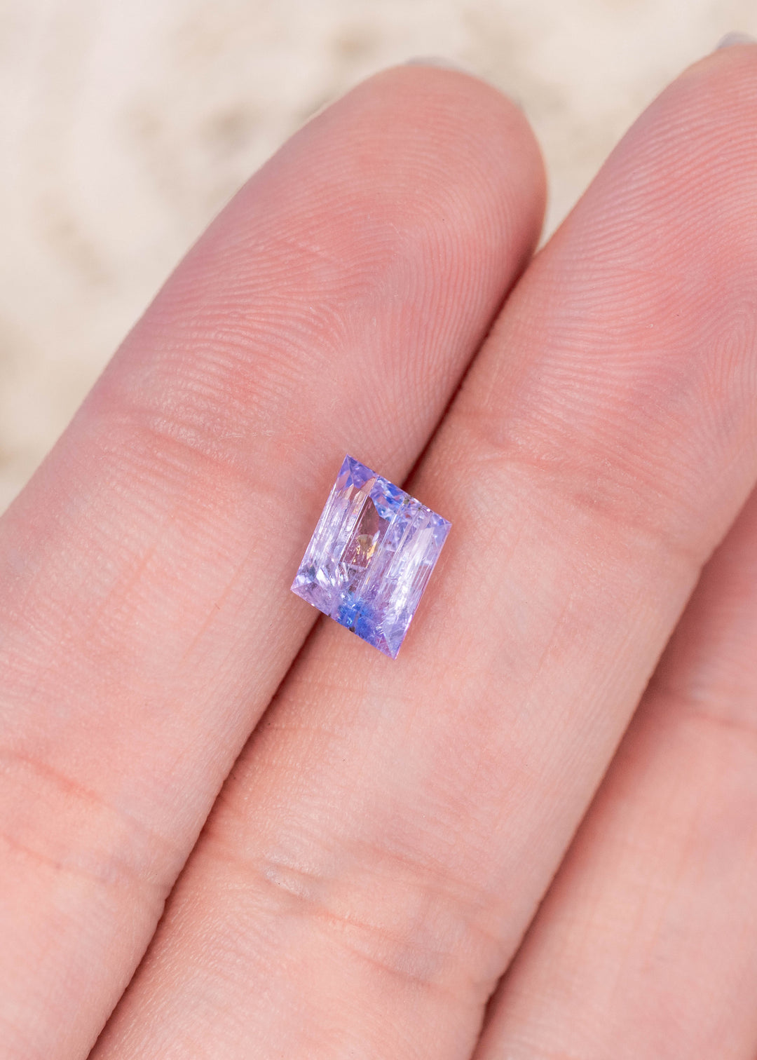 Loose 1.67ct emerald cut Tanzanite resting on fingers displaying mermaid purple blue green hues from Merelani Hills Tanzania