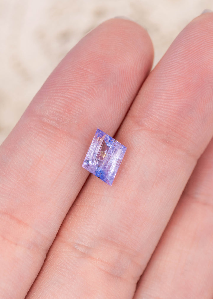 Loose 1.67ct emerald cut Tanzanite resting on fingers displaying mermaid purple blue green hues from Merelani Hills Tanzania