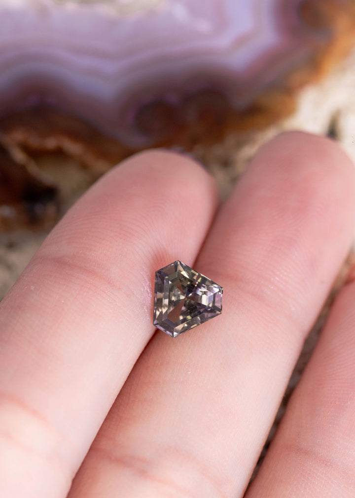 Loose 1.87ct peach lavender Tanzanite resting on fingers displaying custom calf head step cut brilliance from Merelani Hills Arusha Region