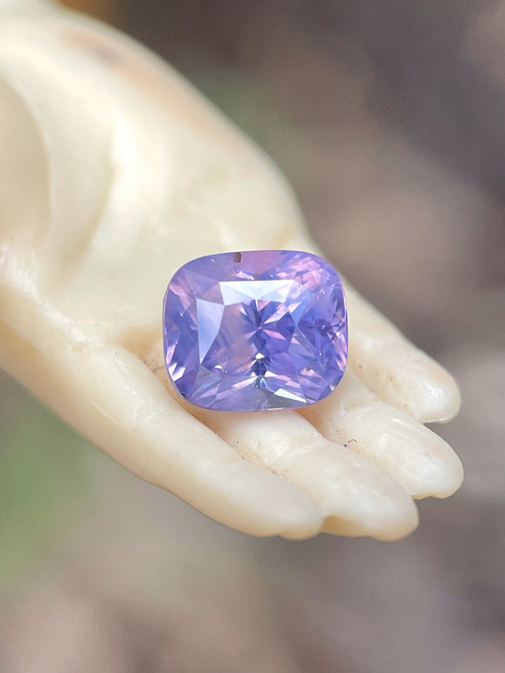 A stunning 2.00-carat opalescent pink and violet sapphire placed delicately on a hand sculpture, showcasing its exceptional brilliance and cushion mix cut. Natural and untreated gemstone from Sri Lanka.