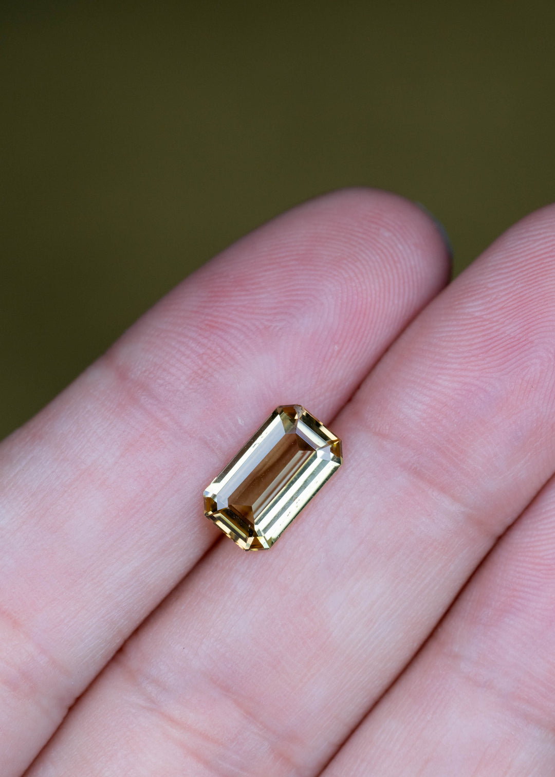 Natural 2.06 carat untreated yellow-green tanzanite displayed on fingertips to illustrate size and precision geometric faceting.