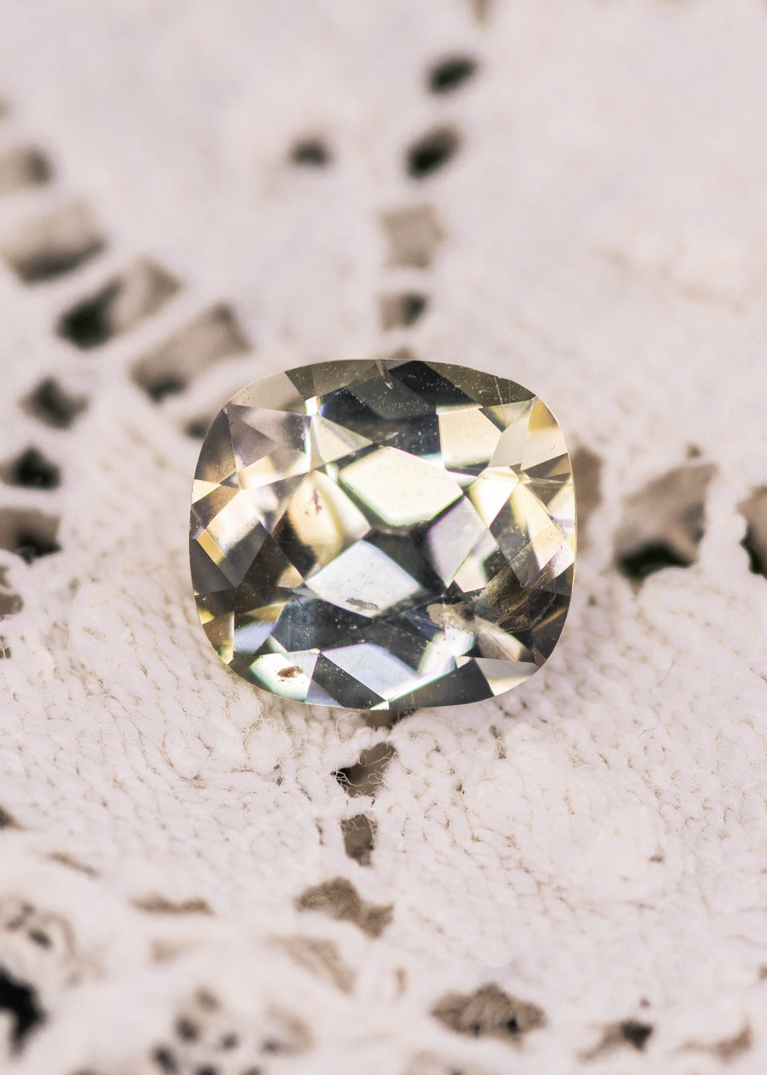 Yellow green Tanzanite cushion brilliant cut gemstone photographed on textured white fabric, showing natural color zoning and crisp facets of an untreated 2.17 carat Tanzanite from Merelani Hills, Tanzania