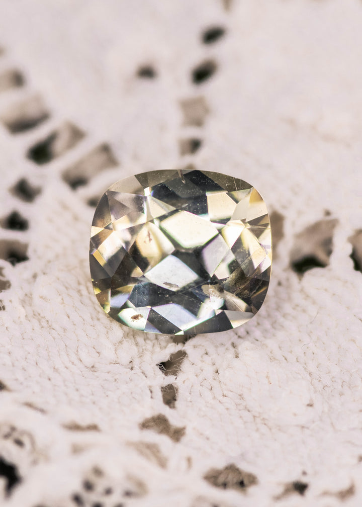 Yellow green Tanzanite cushion brilliant cut gemstone photographed on textured white fabric, showing natural color zoning and crisp facets of an untreated 2.17 carat Tanzanite from Merelani Hills, Tanzania