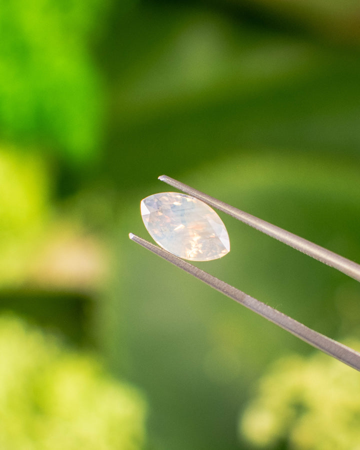 2.18 carat opalescent peach and gray sapphire held in gemstone tweezers under natural sunlight, highlighting brilliance and soft color blending in a precision marquise mixed cut, untreated sapphire from Ratnapura, Sri Lanka.