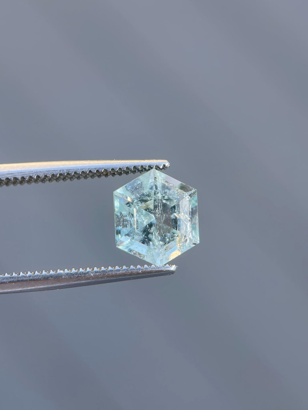 A stunning 2.20ct Green Beryl held in gem tweezers, displaying its precise step-cut facets against a neutral background.