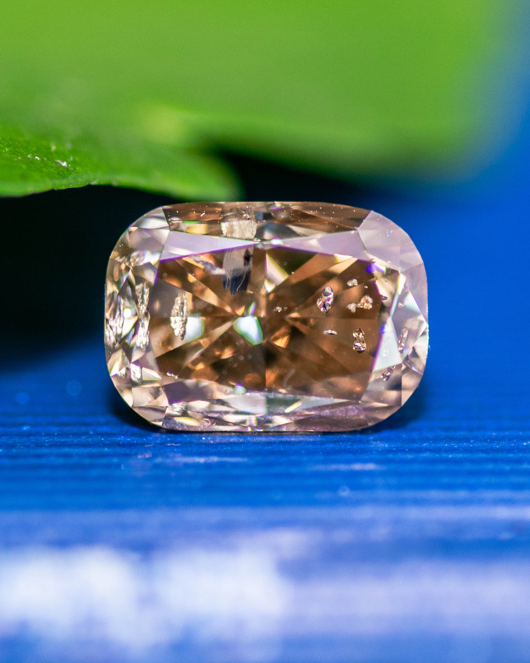 Close-up of a 2.20 carat fancy brown diamond from Argyle Mines, Australia, on a vivid blue background. The elongated cushion cut highlights intricate faceting, natural untreated color, and internal inclusions characteristic of Argyle diamonds.