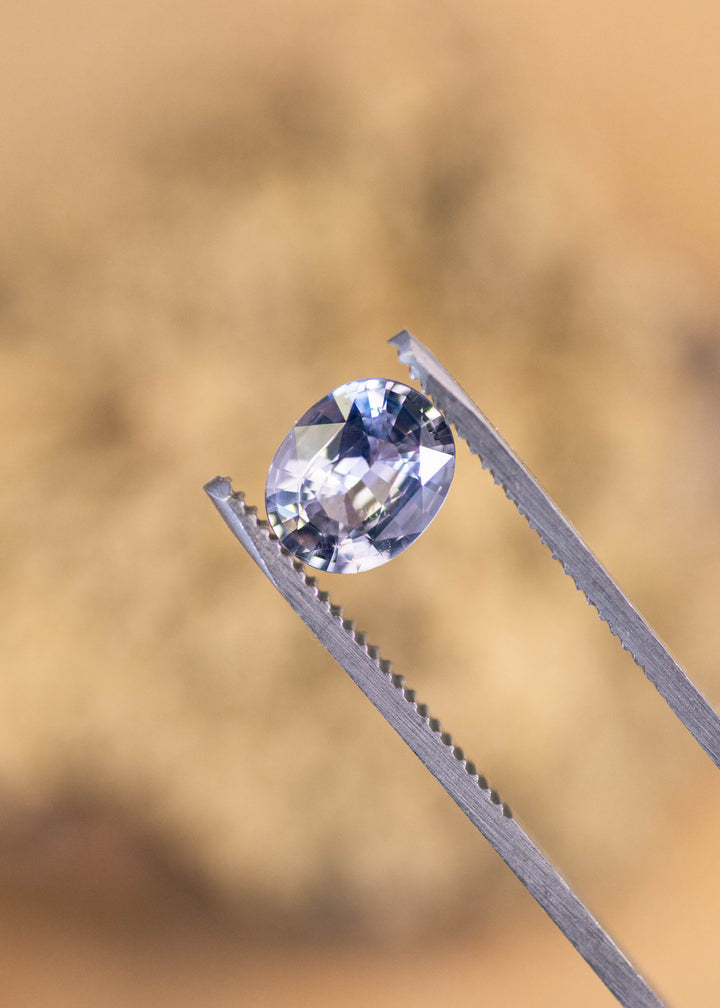 Oval mix cut 2.25ct gray clear pink sapphire held in gem tweezers, untreated Sri Lankan sapphire highlighting precision faceting and clarity
