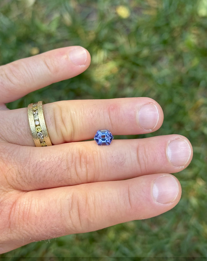Hand shot displaying a 2.28ct hexagonal Tanzanite from Merelani Hills, Tanzania, with strong teal and violet color play under natural lighting.