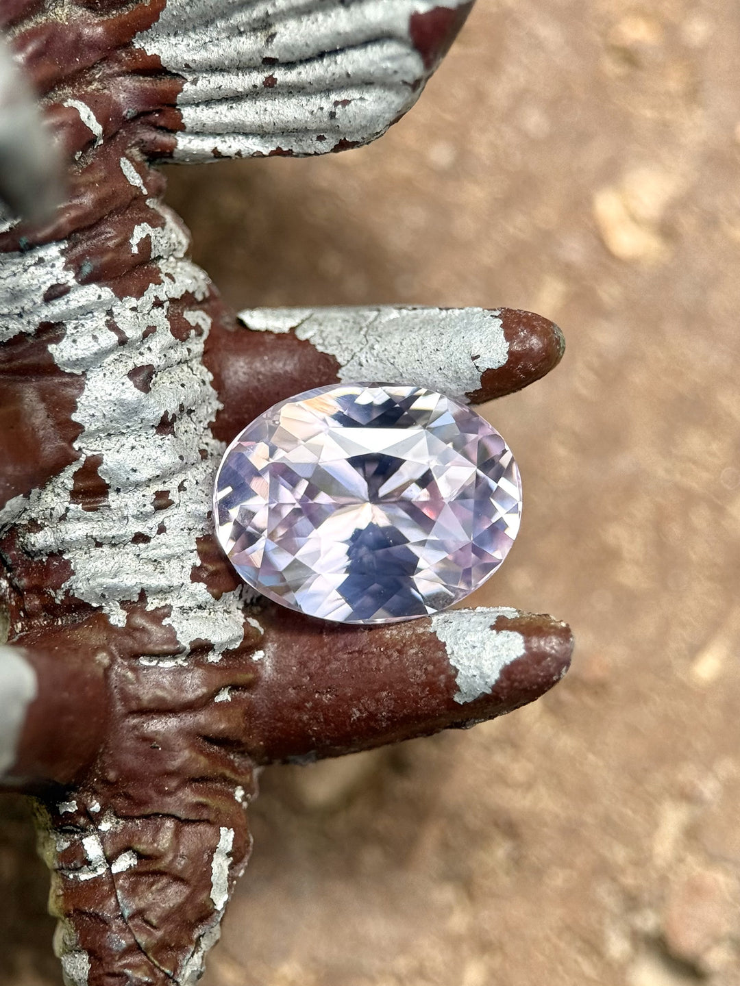 2.52ct unheated opalescent pink sapphire displayed on textured rustic iron, showcasing its vivid oval brilliance and Sri Lankan origin.