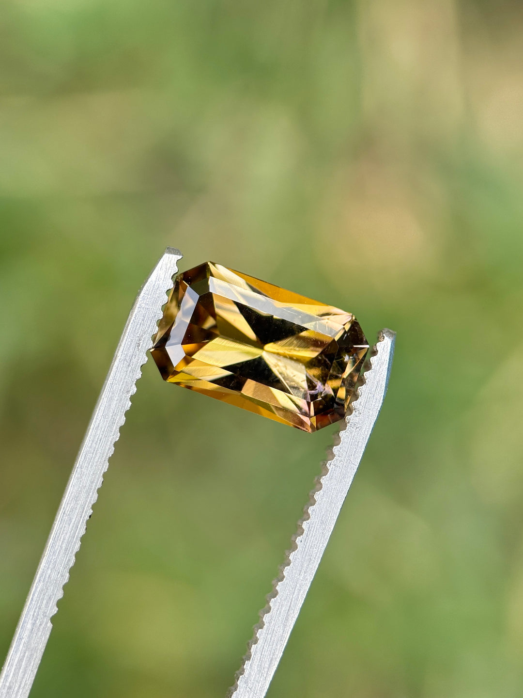 Close-up of 2.63CT Tanzanite held in gemstone tweezers under natural daylight, highlighting its fancy color mix of purple, pink, and golden yellow in a custom octagon radiant cut, ethically sourced from Merelani Hills, Tanzania.