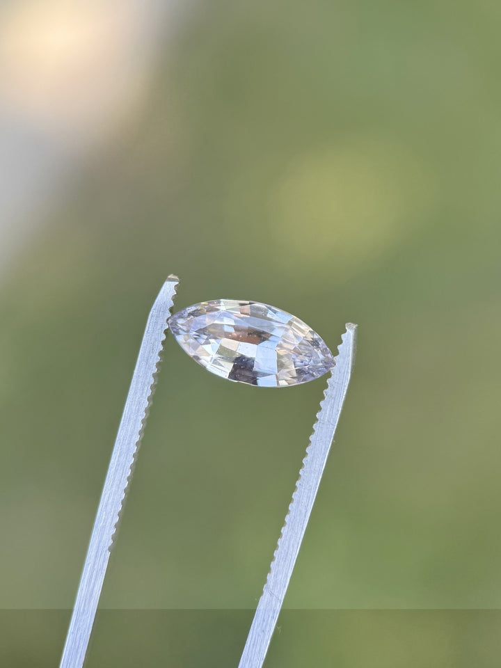 Natural 2.68CT light lilac sapphire held in gemstone tweezers against soft green background, displaying clean facets and silvery violet tones, no-heat marquise mixed cut gem from Madagascar.