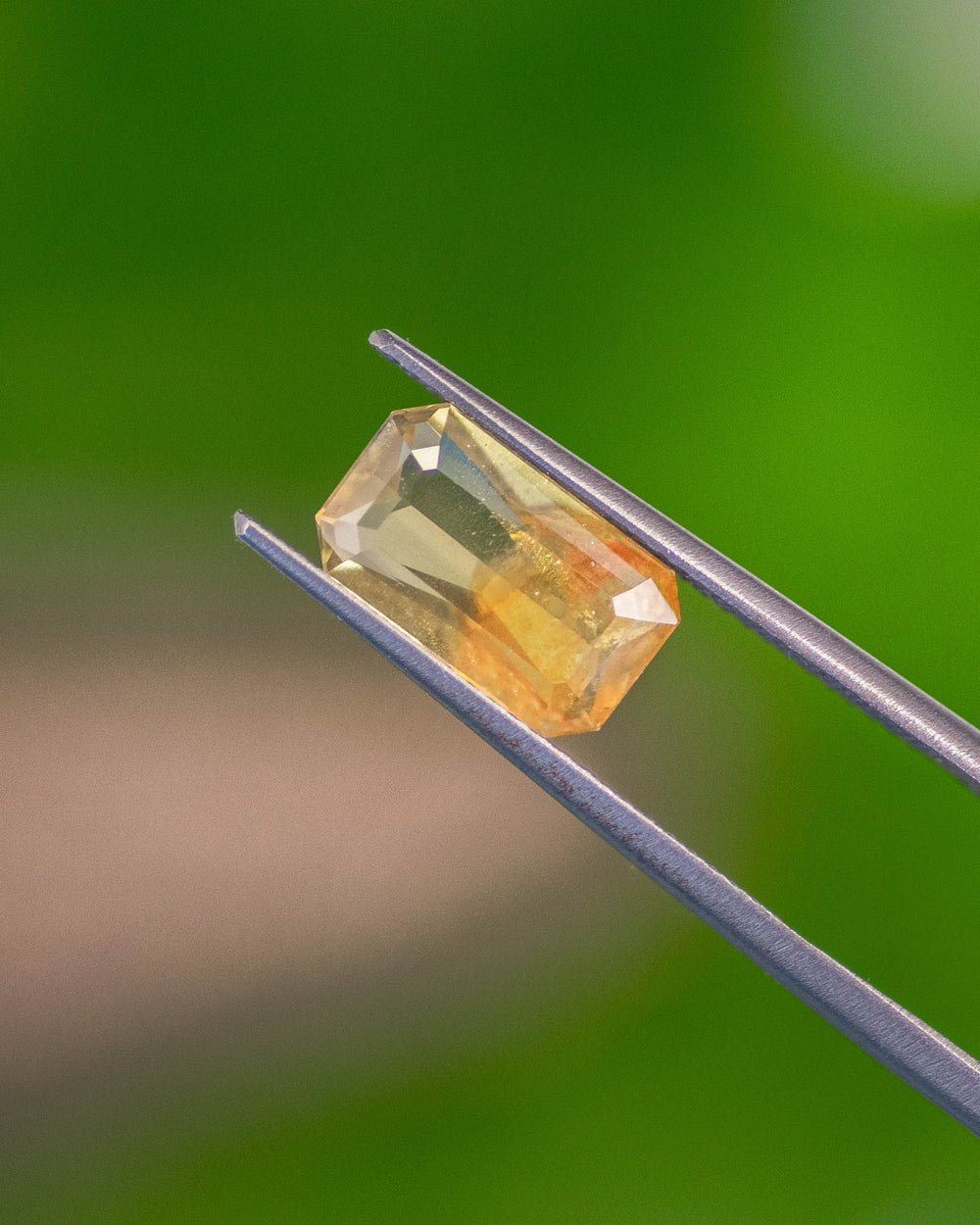 Macro image of 2.74CT parti sapphire held in gemstone tweezers, showing color zoning and fine craftsmanship of the custom octagonal step cut, unheated sapphire from Umba River, Tanzania.