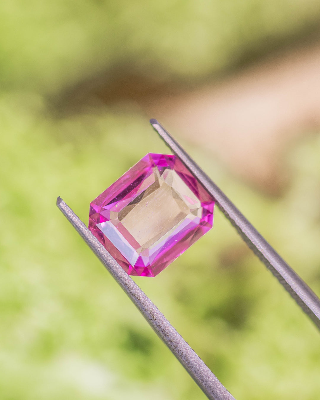 3.01 carat pink sapphire held in gemstone tweezers against a natural green background, showcasing vivid color and geometric symmetry of the custom octagonal portrait cut, untreated gem from Sakaraha, Madagascar.