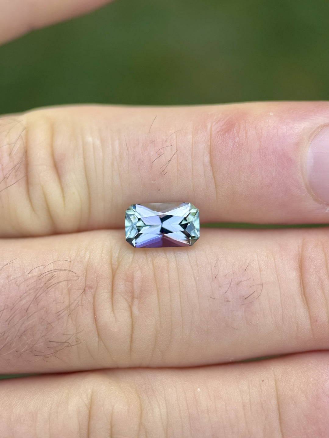 Mermaid-color Tanzanite gemstone in modified radiant cut resting across fingertips with vivid reflections