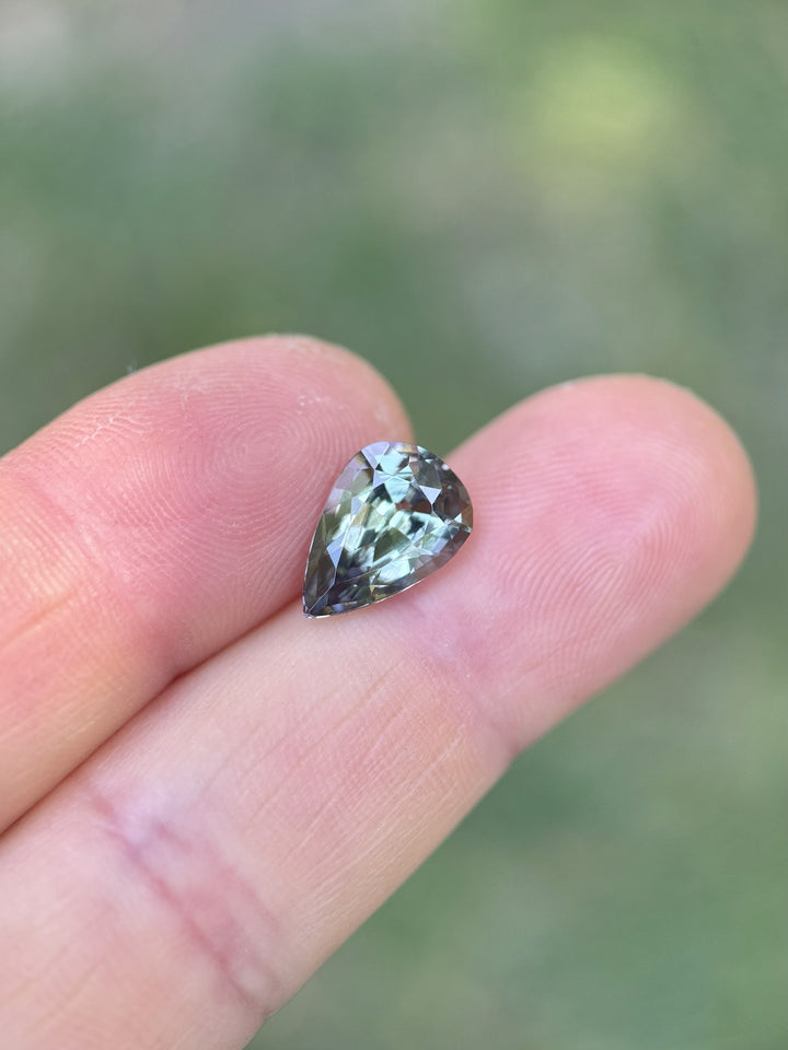 Handheld view of Tanzanite with custom mix cut showing teal, purple, and green flashes across the pear shape