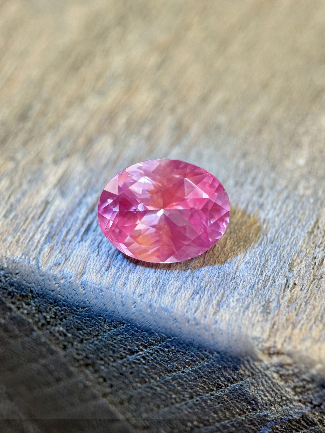Natural untreated 4.04 carat sapphire in vivid pink tones displayed on a wooden surface, showcasing high brilliance and facet symmetry, precision oval cut from Madagascar.